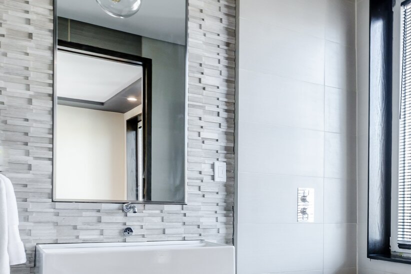 Weißes Badezimmer mit rechteckigen Spiegel an einer Steinwand.