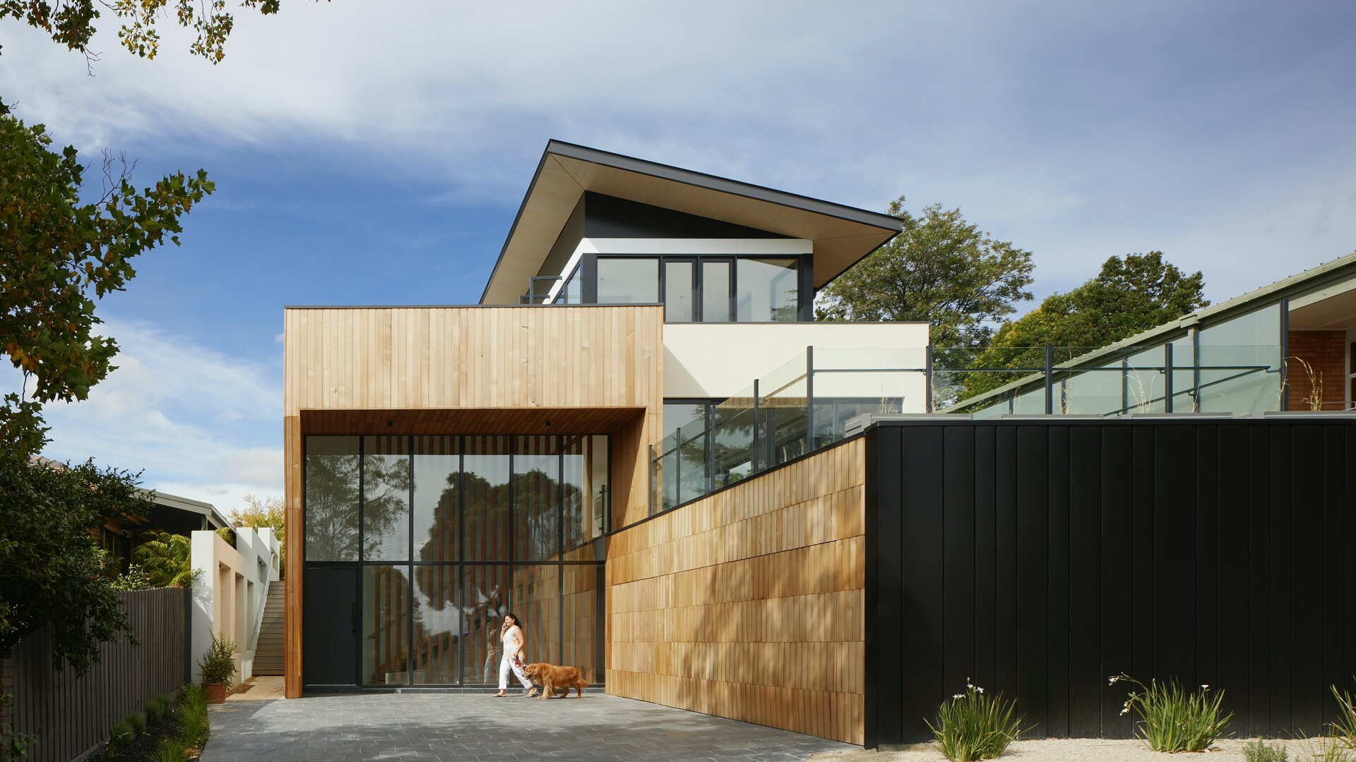 Vista esterna di una casa moderna con elementi costruttivi di raccordo effetto legno chiaro e nero ed elementi in vetro.