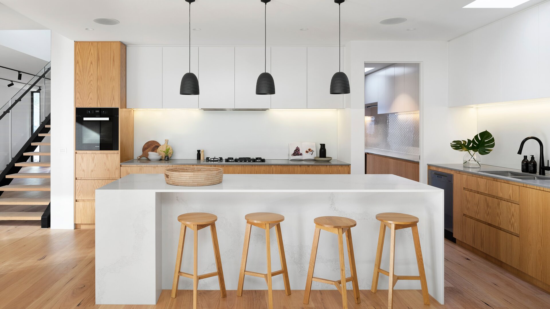Moderna cucina bianca con elementi in legno, isola bianca e sgabello in legno.